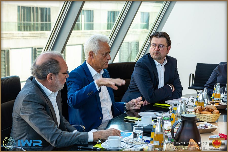 Briefing an einem Konferenztisch: eine Person erläutert etwas, die anderen hören konzentriert zu, Unterlagen vor sich.