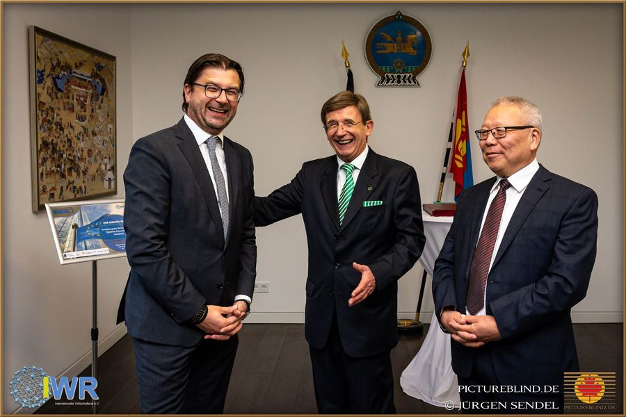 Begrüßung bei einem diplomatischen Empfang, im Hintergrund Wappen und Flagge.