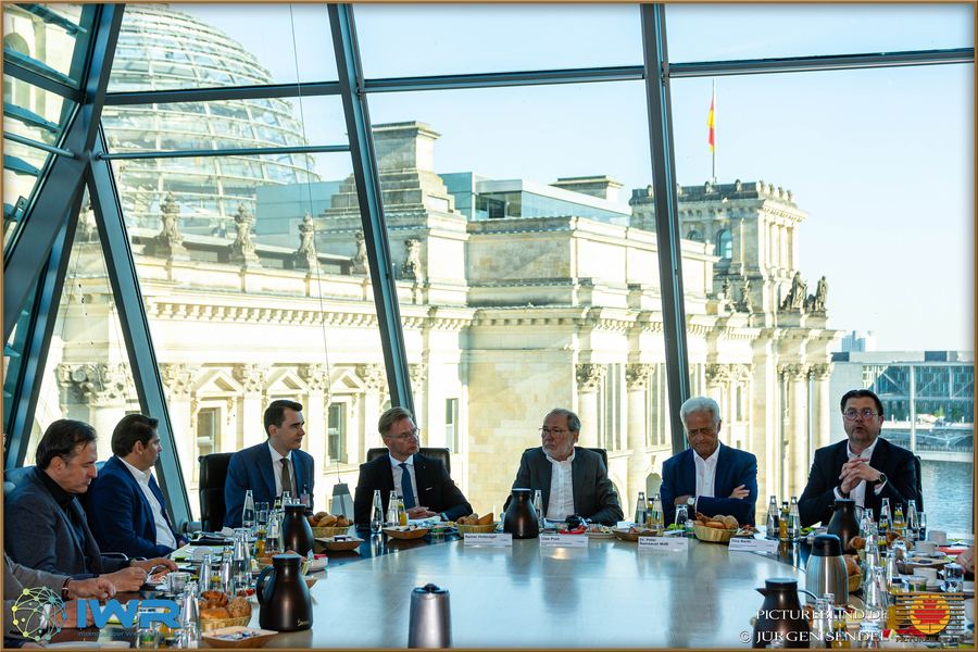 Gesprächsrunde an einem langen Tisch, durch die Glasfassade ist das Reichstagsgebäude zu sehen.