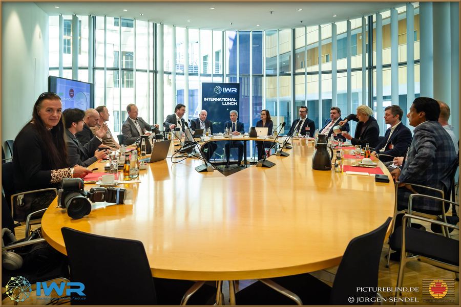 Runder Konferenztisch mit Teilnehmenden, vor einer hohen Fensterfront – eine geschlossene Runde.