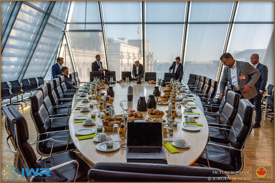 Langer, eingedeckter Konferenztisch unter einer Glaskuppel, vorbereitet für eine Gesprächsrunde.